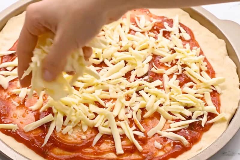 sprinkling shredded cheese over pizza sauce. on dough.