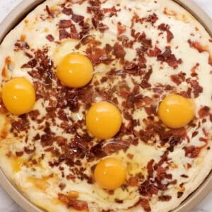 5 raw eggs cracked over top of a partially baked breakfast pizza.