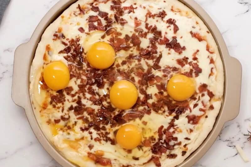 5 raw eggs cracked over top of a partially baked breakfast pizza.