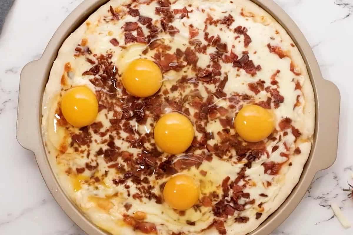 5 raw eggs cracked over top of a partially baked breakfast pizza.