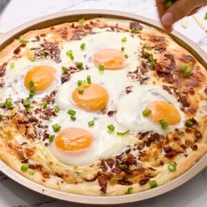 sprinkling chives over a baked breakfast pizza in a pizza pan.