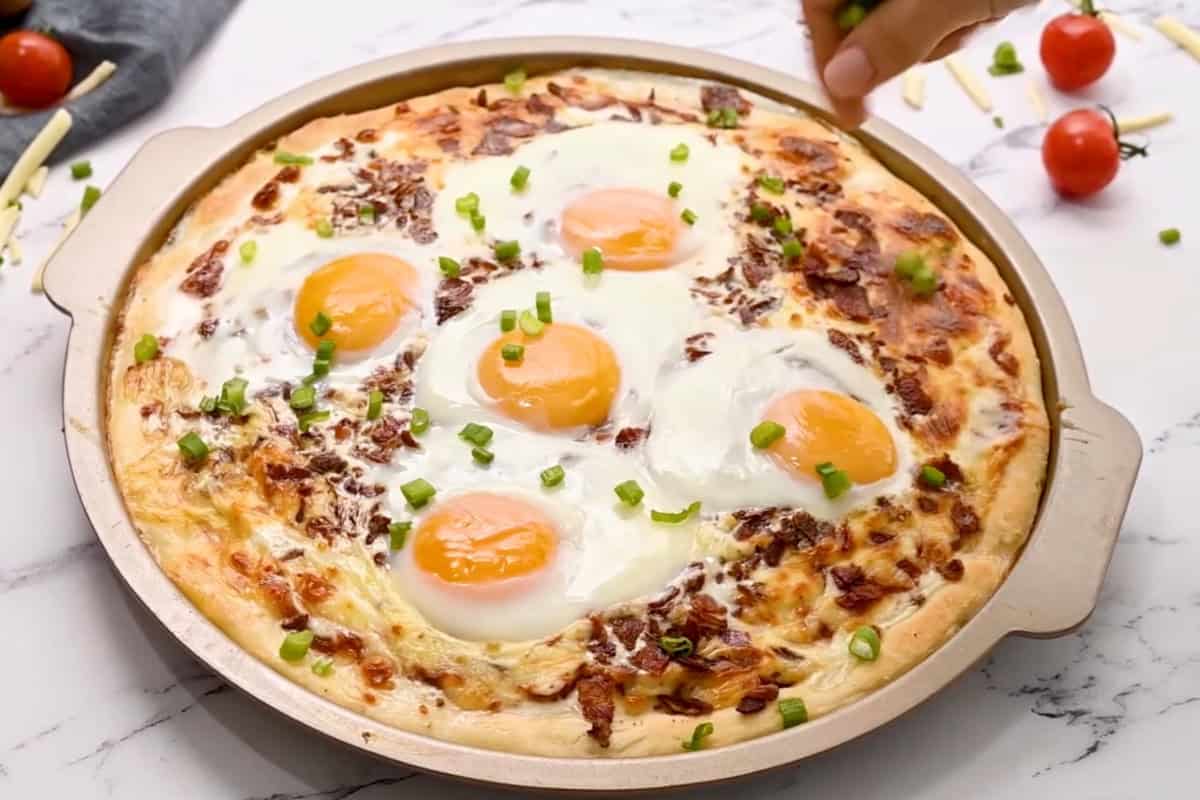 sprinkling chives over a baked breakfast pizza in a pizza pan.