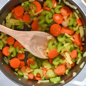 sauteed veggies in a dutch oven with a wooden spoon.