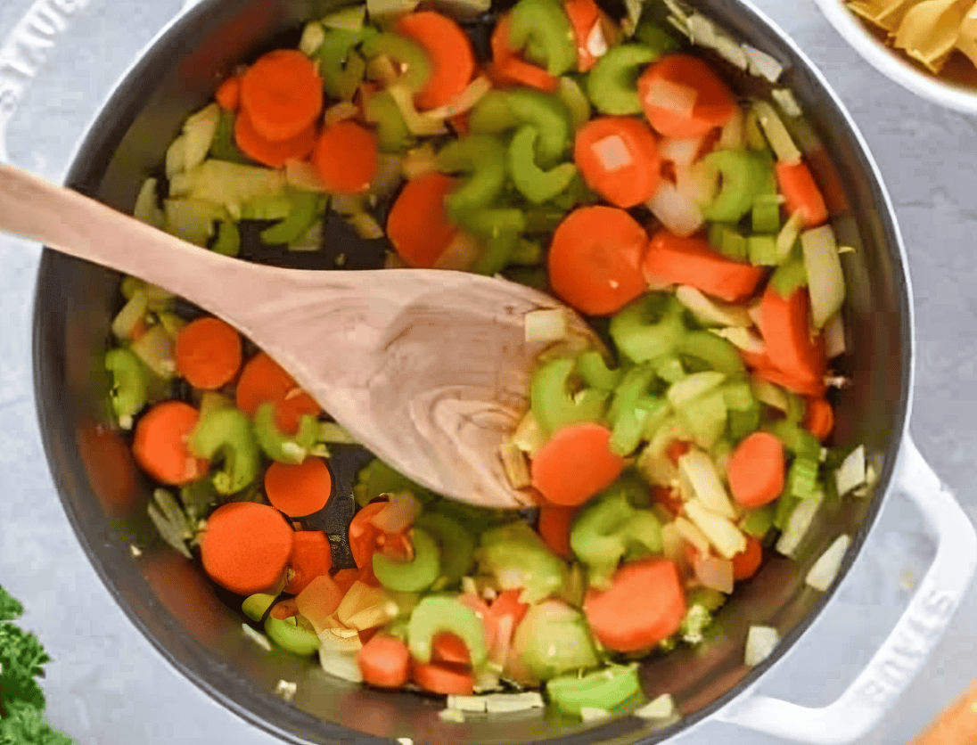 sauteed veggies in a dutch oven with a wooden spoon.