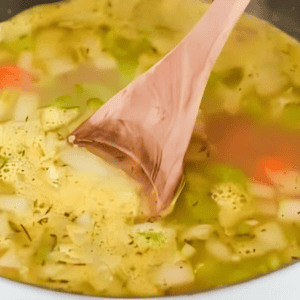 stirring homemade chicken noodle soup with a wooden spoon.