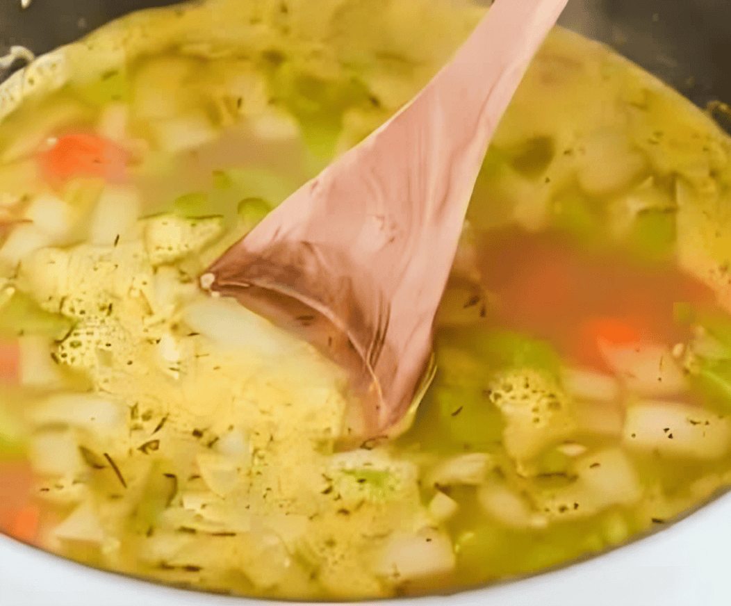 stirring homemade chicken noodle soup with a wooden spoon.