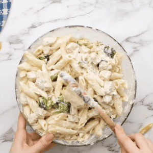 chicken, penne, broccoli, and cheese sauce mixed in a glass bowl.