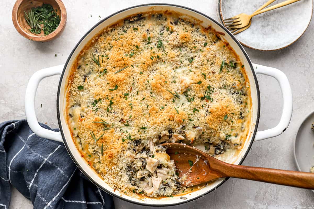 Baked chicken wild rice casserole in a white dish, with a wooden spoon for serving.