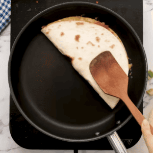 A chicken quesadilla is being cooked in a pan.