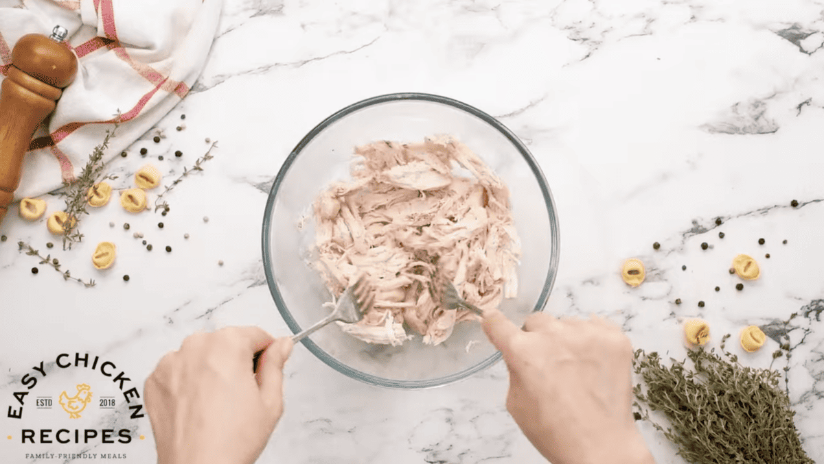 Chicken is being shredded in a bowl.