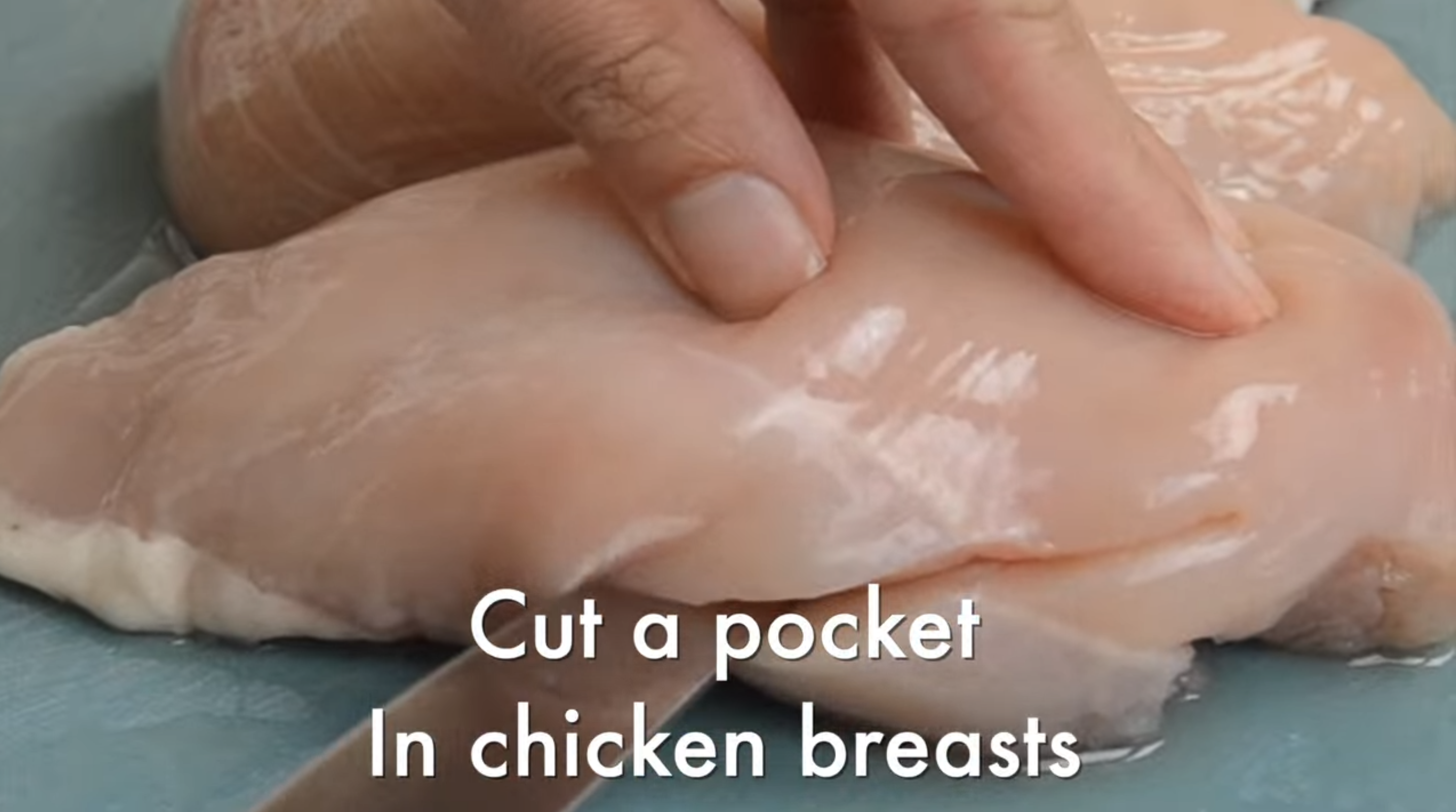 A chicken breast is being sliced with a knife. 