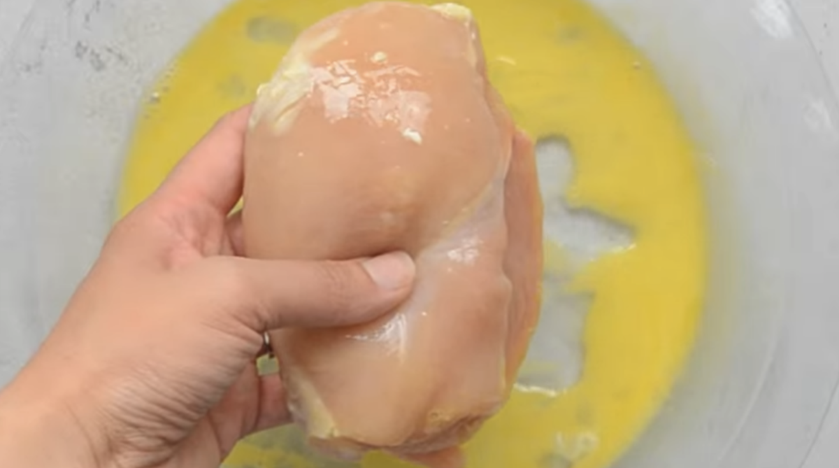 A chicken breast is being coated in egg wash.