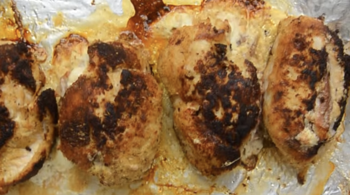 Four stuffed chicken breasts are lined up on a baking sheet.