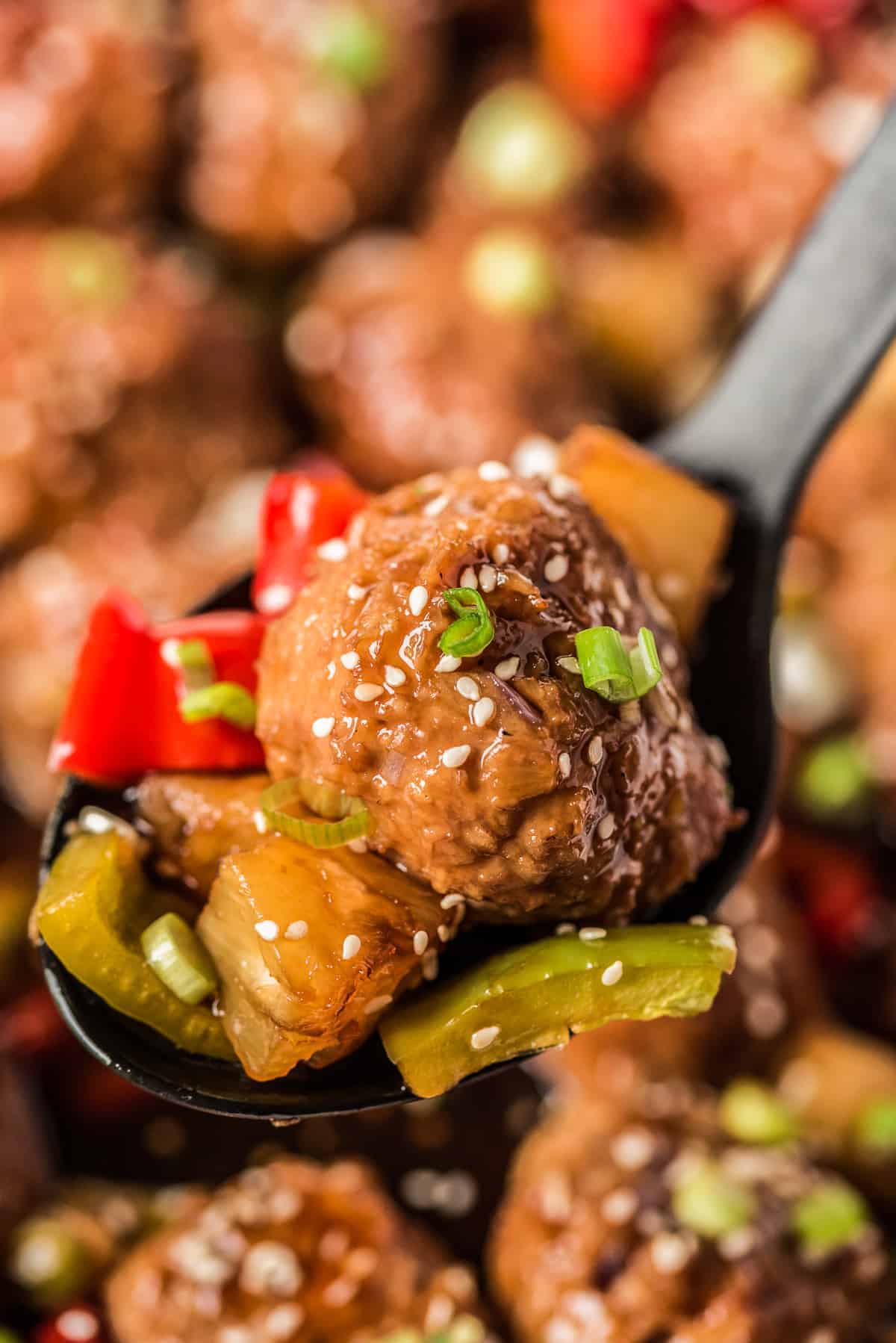 Spoon lifting a meatball with bites of pineapple and bell pepper.