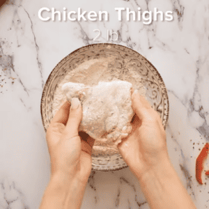Chicken thighs are being coated in flour.