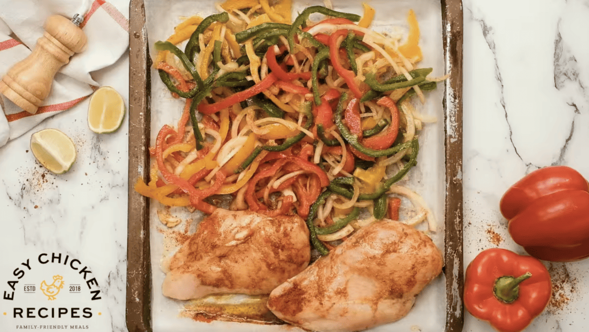 Uncooked chicken fajitas are spread on a baking sheet. 