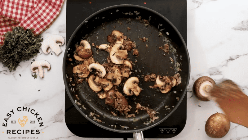 Mushrooms, onions and herbs are in a skillet.