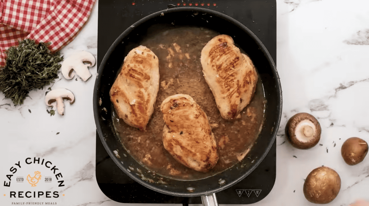 Chicken breasts and white wine are cooking in a pan.