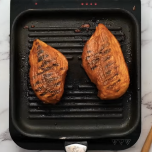 Grilled chicken breasts are on a grill.