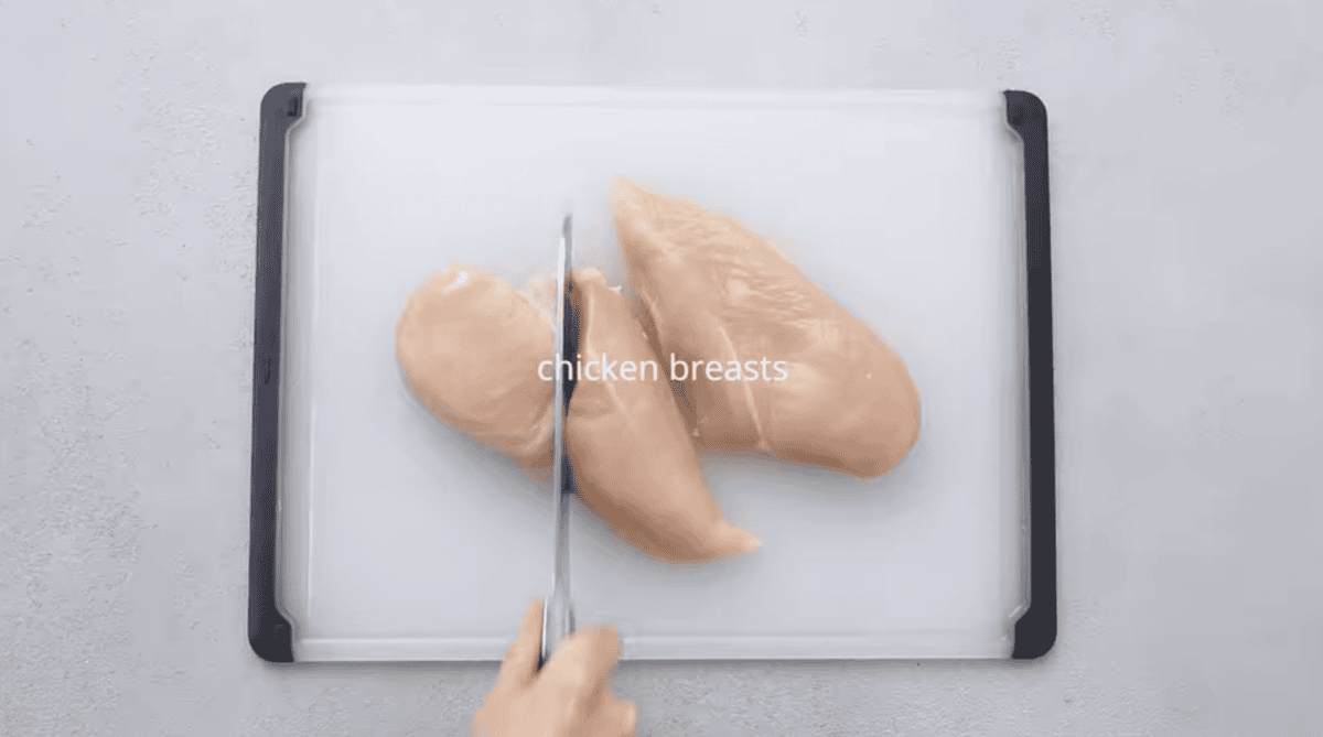 A chicken breast is being sliced in half. 