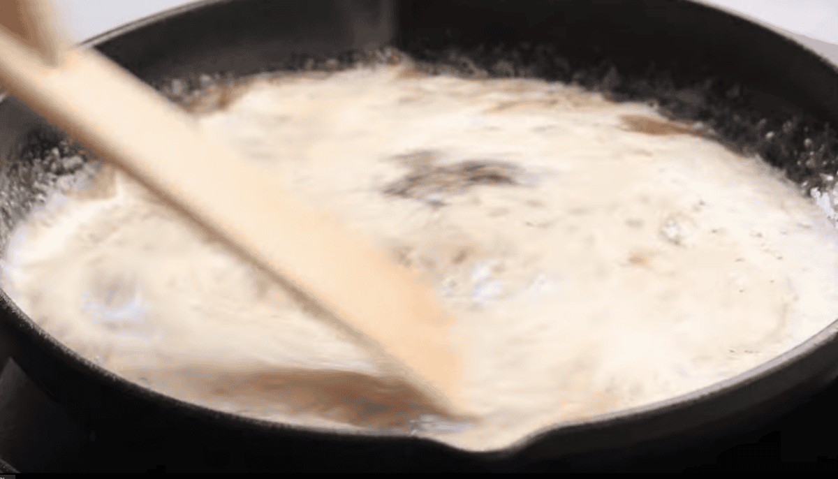 Cream is being stirred in a skillet. 