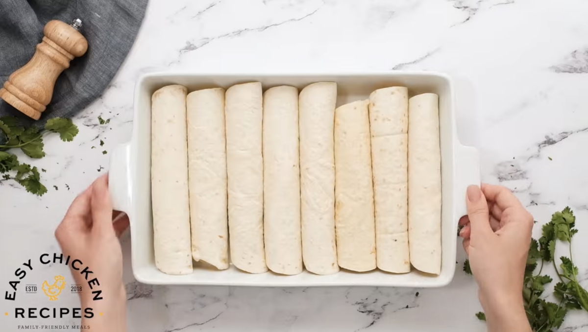 Tortillas are rolled with filling and lined up in a casserole dish. 