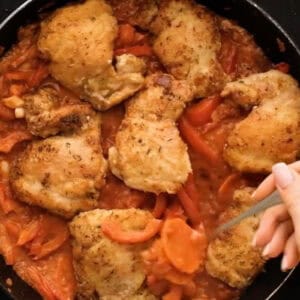 spooning cacciatore sauce over chicken thighs in a pan.