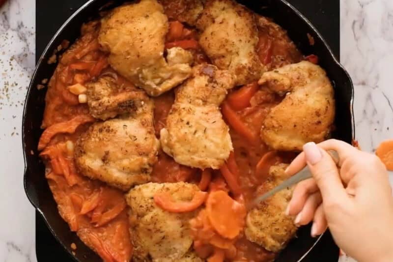 spooning cacciatore sauce over chicken thighs in a pan.