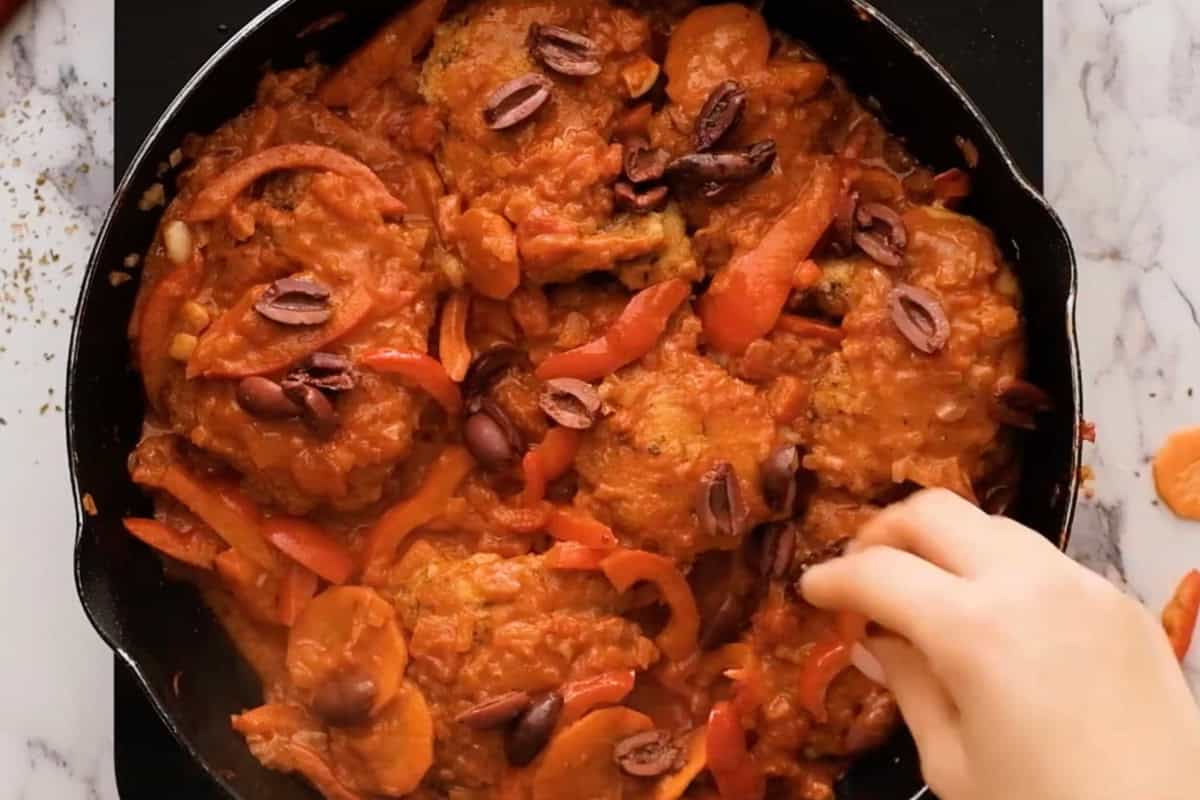 adding olives to a pan of chicken cacciatore.