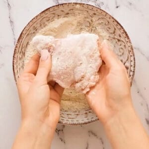 dredging a chicken thigh in seasoned flour.