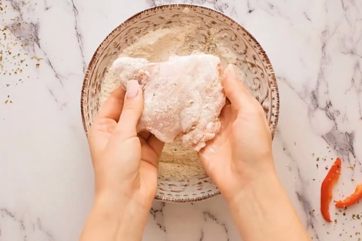 dredging a chicken thigh in seasoned flour.
