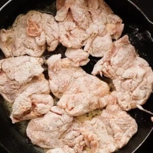 searing dredged chicken thighs in a pan.