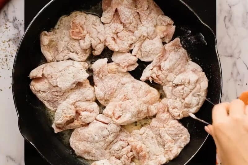 searing dredged chicken thighs in a pan.