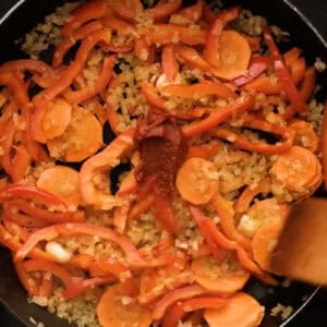 adding tomato paste to diced veggies in a pan.