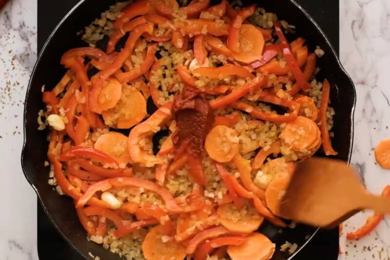 adding tomato paste to diced veggies in a pan.