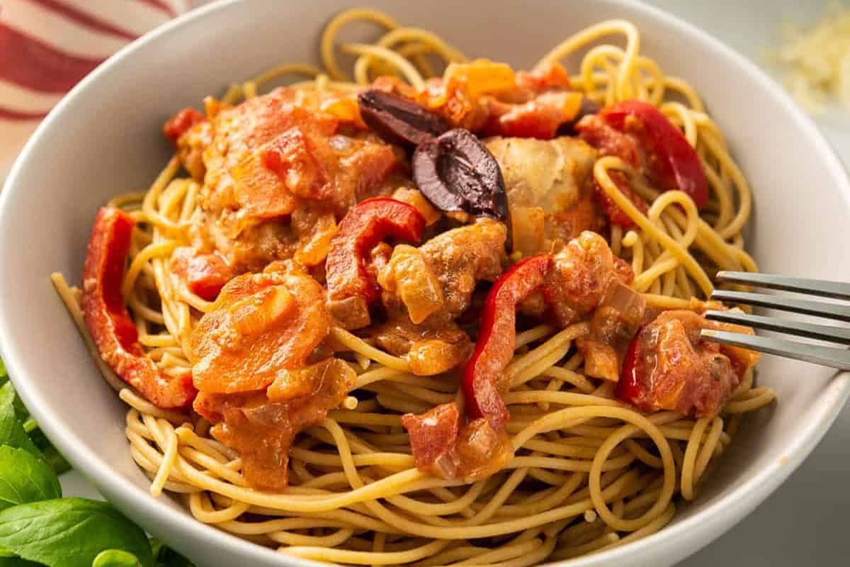 closeup of a serving of chicken cacciatore over pasta in a bowl.