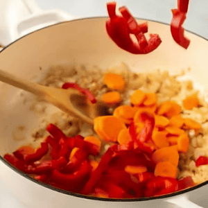 adding chopped carrots and peppers to a dutch oven.