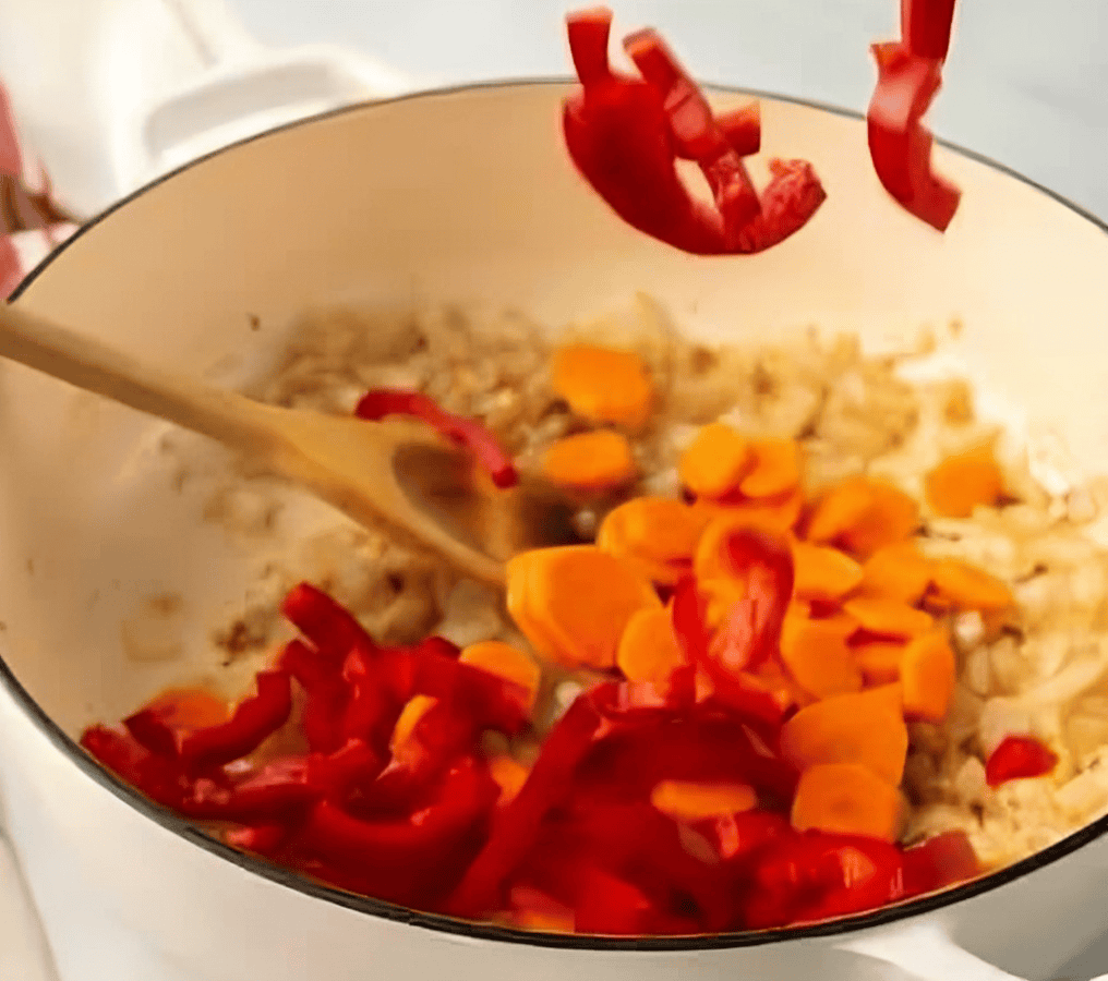 adding chopped carrots and peppers to a dutch oven.