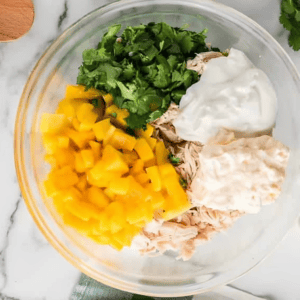 yogurt, mayo, mango, and cilantro over shredded cooked chicken in a glass bowl.