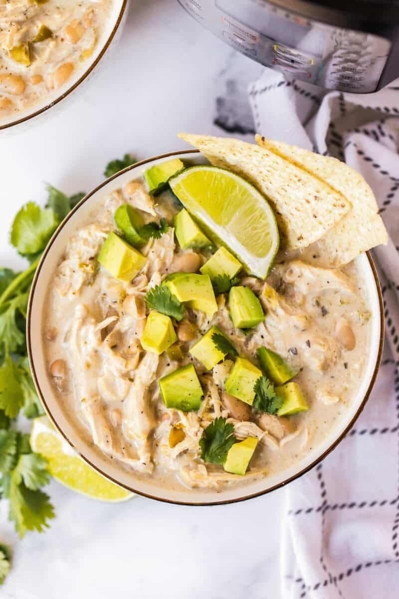 bowl of instant pot white chicken chili garnished with avocado and chips