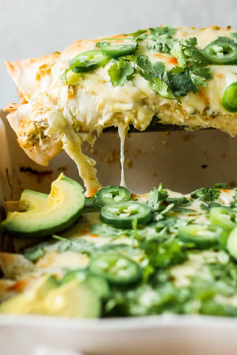 lifting up chicken enchiladas with cheese garnished in pan