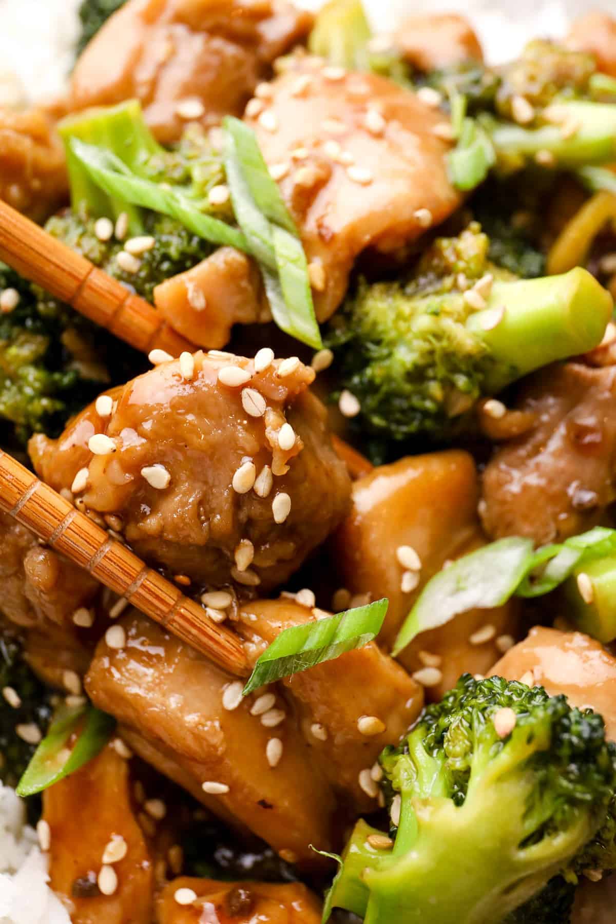 up close image of teriyaki chicken thighs garnished with sesame seeds being picked up by chopsticks