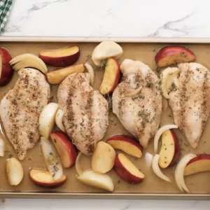 Chicken, apples and onions are spread on a baking sheet.