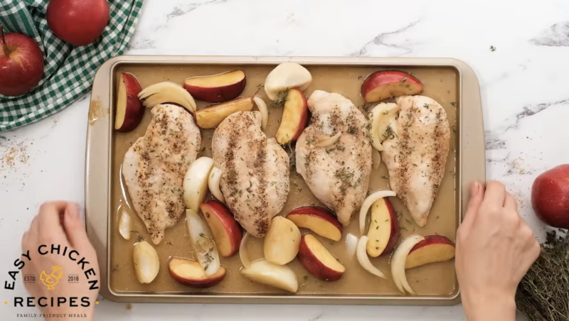 Chicken, apples and onions are spread on a baking sheet.