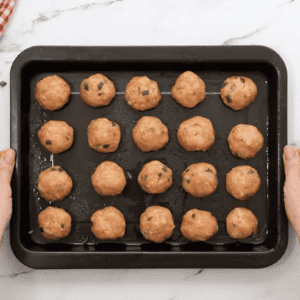 Raw chicken meatballs are on a baking sheet.