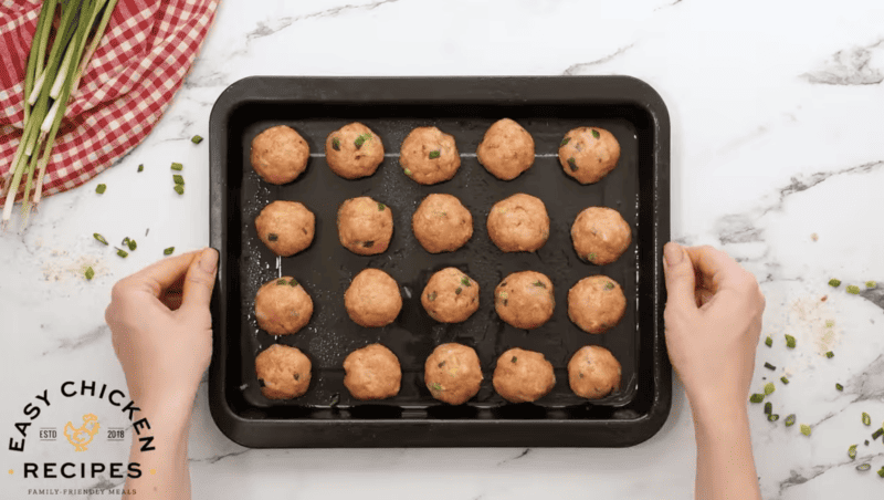 Raw chicken meatballs are on a baking sheet.