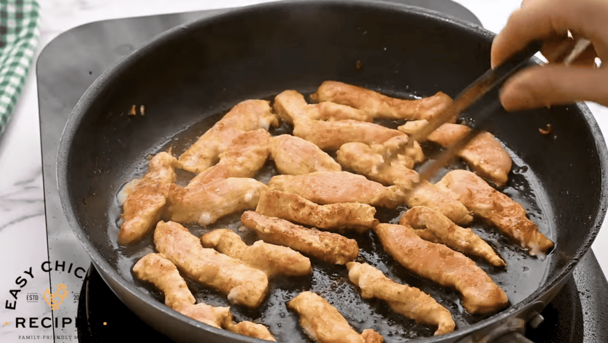 Chicken is cooking in a skillet. 