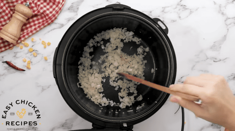 A person is stirring onions in an instant pot.