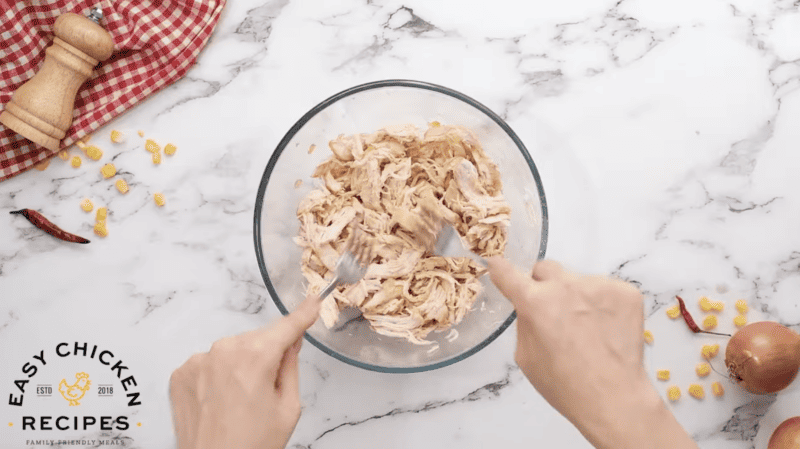 Chicken is being shredded in a bowl.