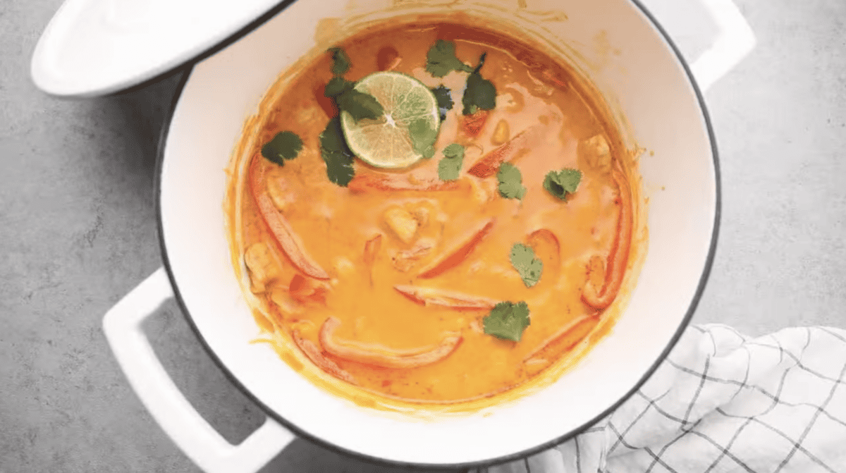 A pot of curry is garnished with cilantro and a lime. 